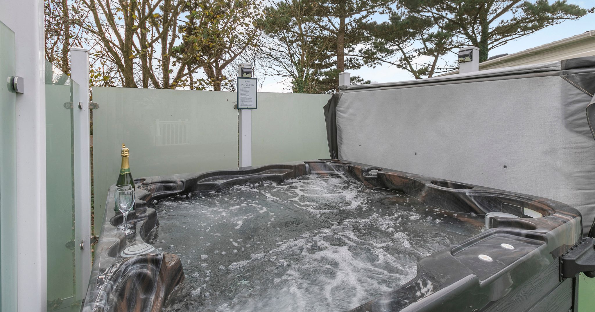 Outdoor hot tub with bubbly water, champagne bottle, and glass by the side