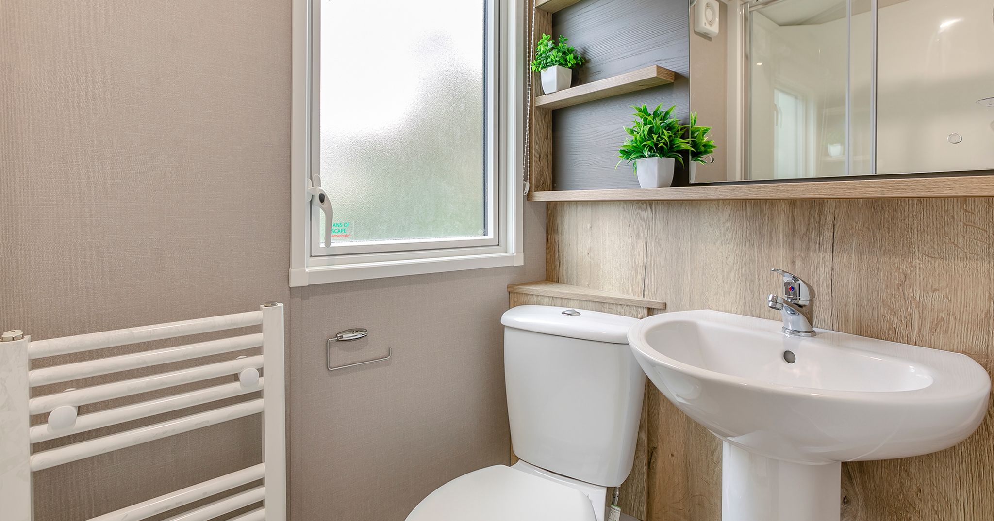 Modern bathroom with white toilet, pedestal sink, frosted window, wooden shelves, and potted green plants.