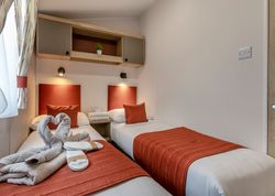 Modern twin bedroom with orange accents and swan-shaped towels on the bed