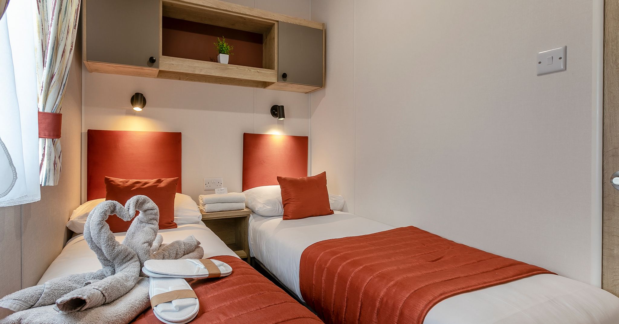 Modern twin bedroom with orange accents and swan-shaped towels on the bed