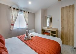 Cozy bedroom with orange accents, bed, window with curtains, and dressing table with mirror