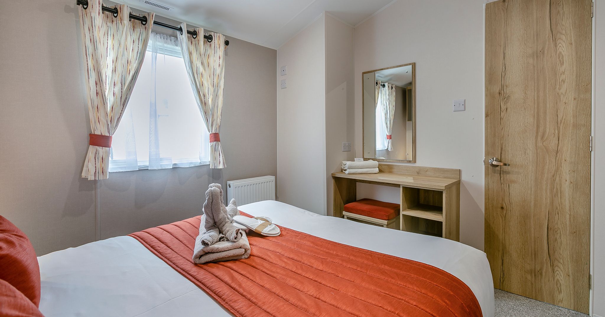 Cozy bedroom with orange accents, bed, window with curtains, and dressing table with mirror