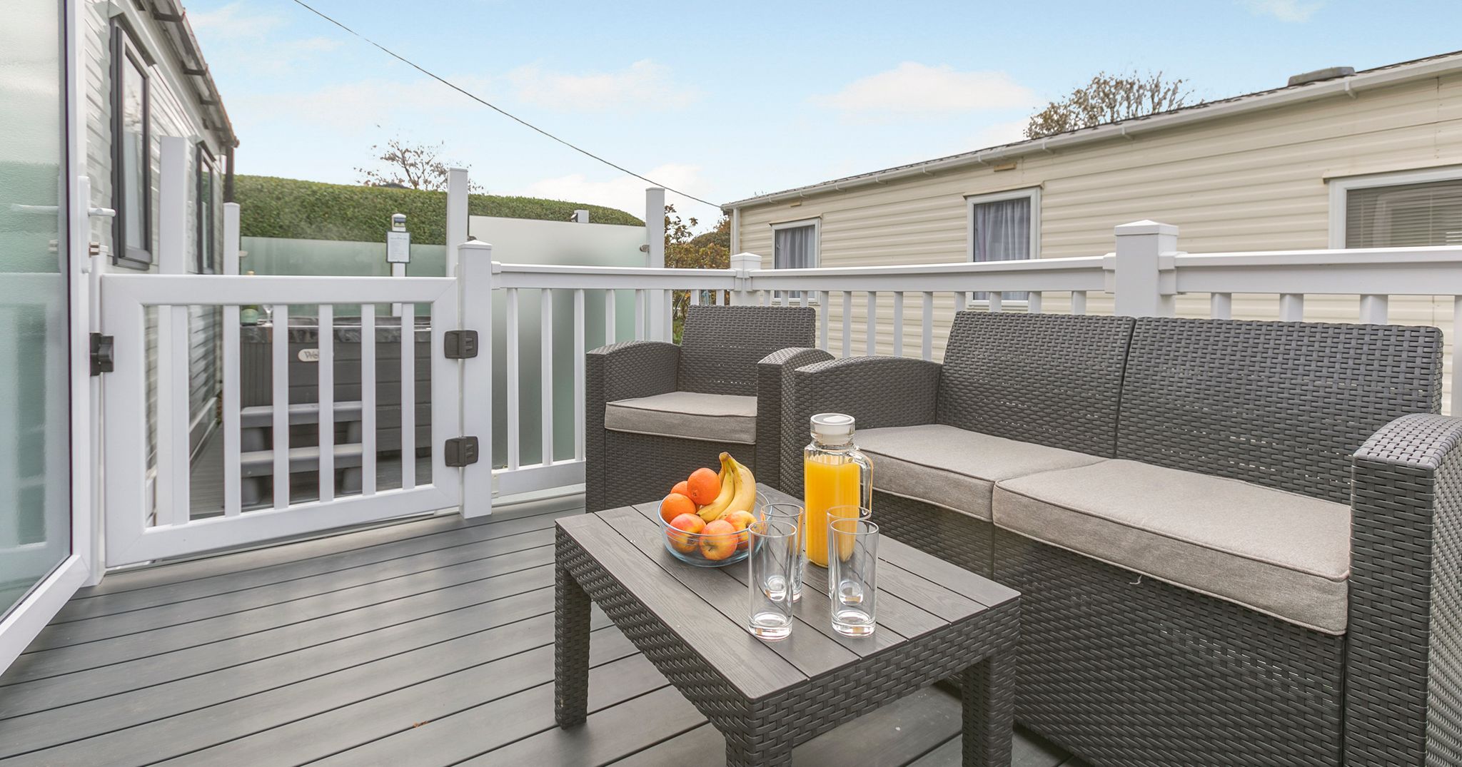 Outdoor patio with rattan furniture, a bowl of fruit, orange juice, and glasses on a table