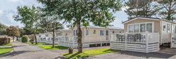 Row of modern mobile homes with white decking under trees in a holiday park.