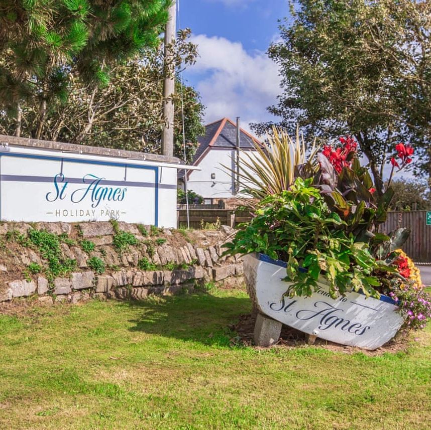 Entrance sign for St Agnes Holiday Park with a decorative boat planter filled with vibrant flowers.