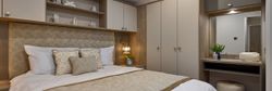 Modern bedroom with beige and white decor, a double bed, built-in wardrobe, and vanity area with mirror