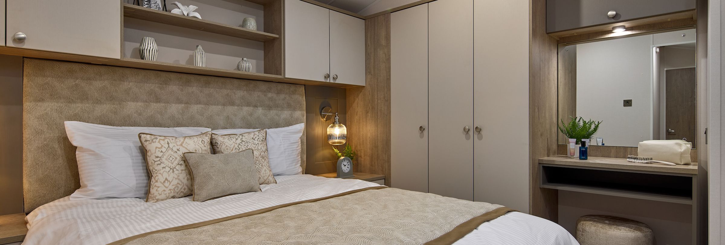Modern bedroom with beige and white decor, a double bed, built-in wardrobe, and vanity area with mirror