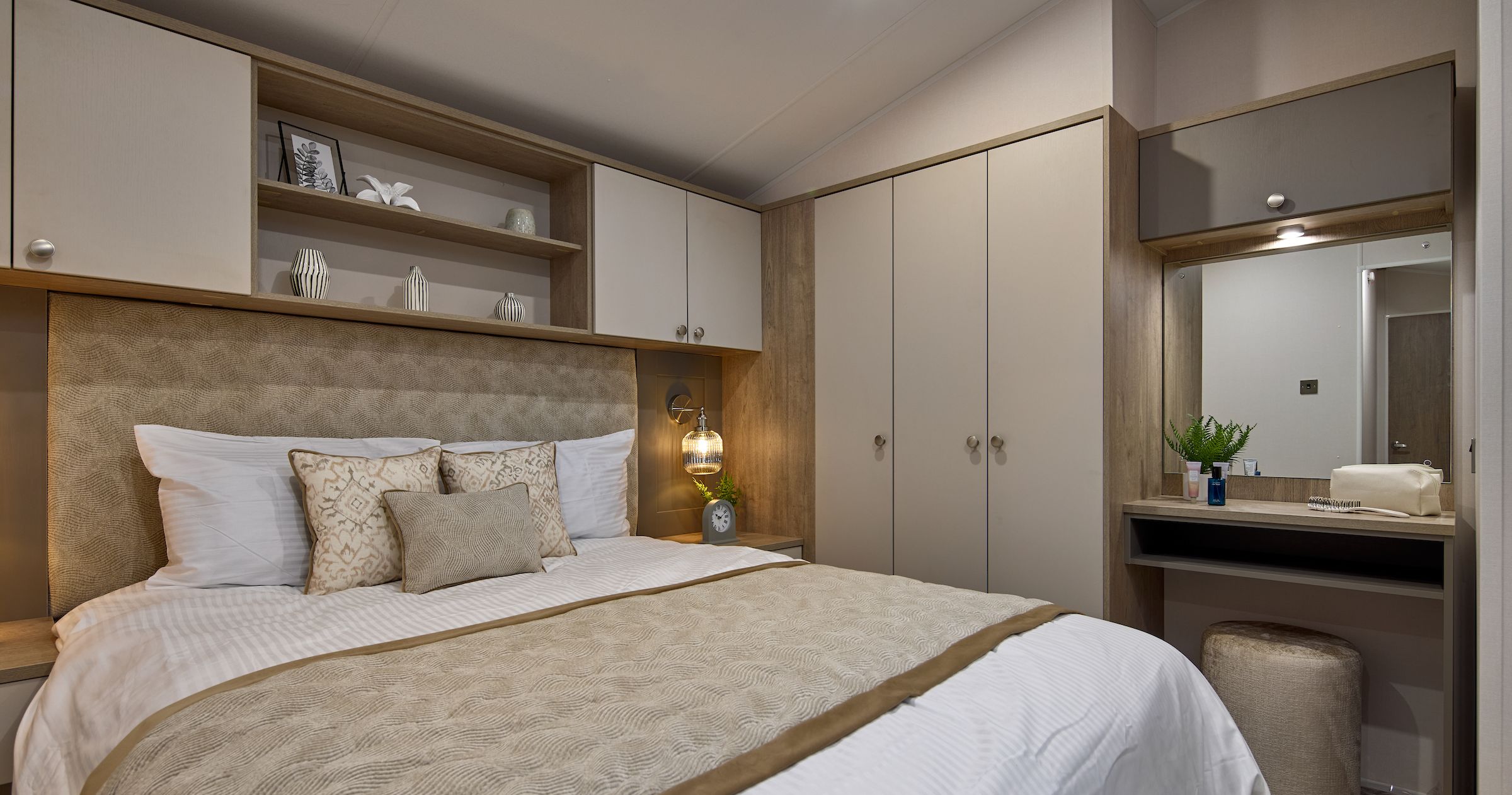 Modern bedroom with beige and white decor, a double bed, built-in wardrobe, and vanity area with mirror
