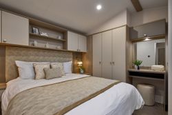 Modern bedroom with beige and white decor, a double bed, built-in wardrobe, and vanity area with mirror