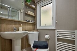 Modern small bathroom with sink, toilet, towel, shelf, and frosted window.