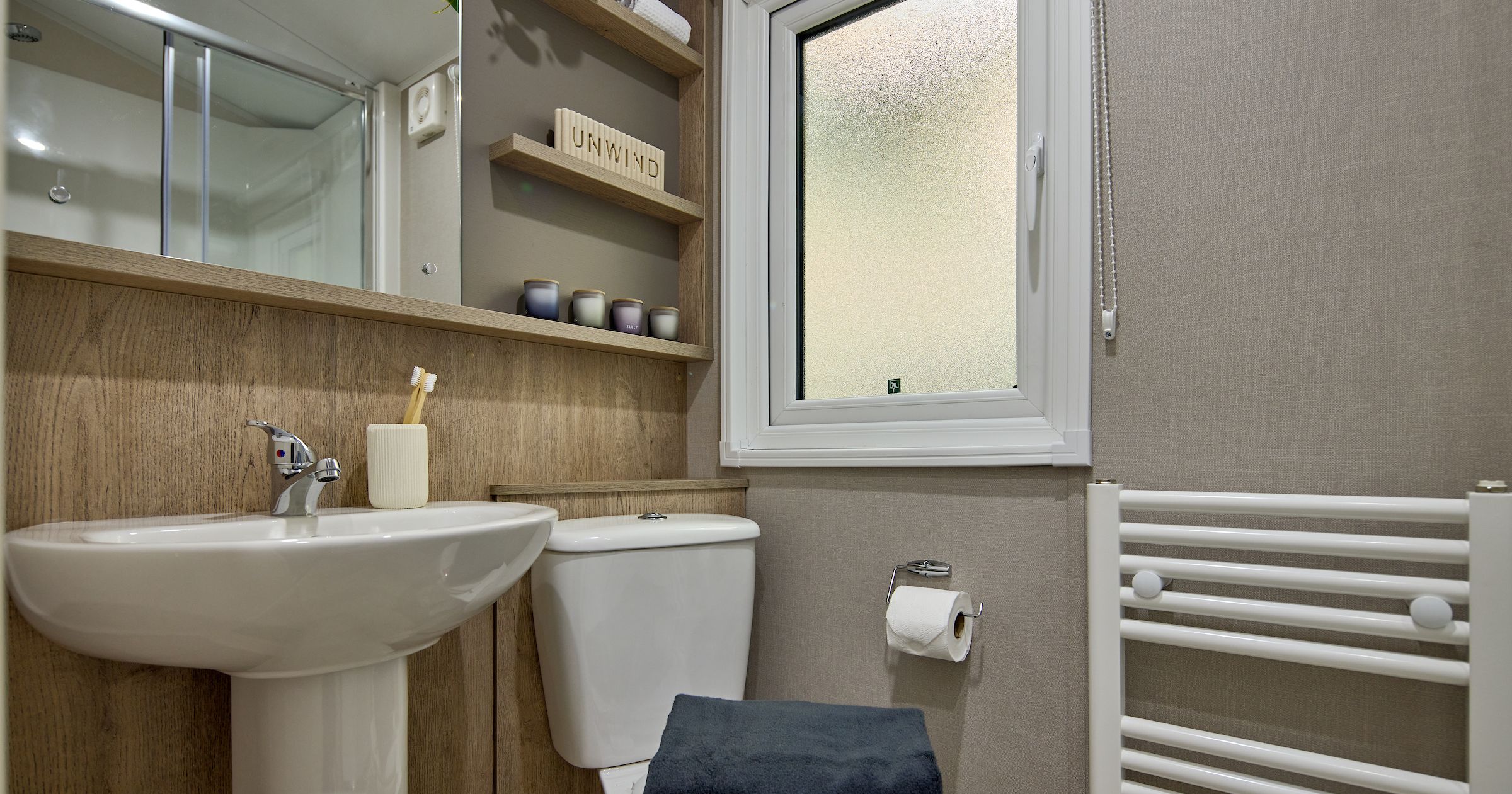 Modern small bathroom with sink, toilet, towel, shelf, and frosted window.