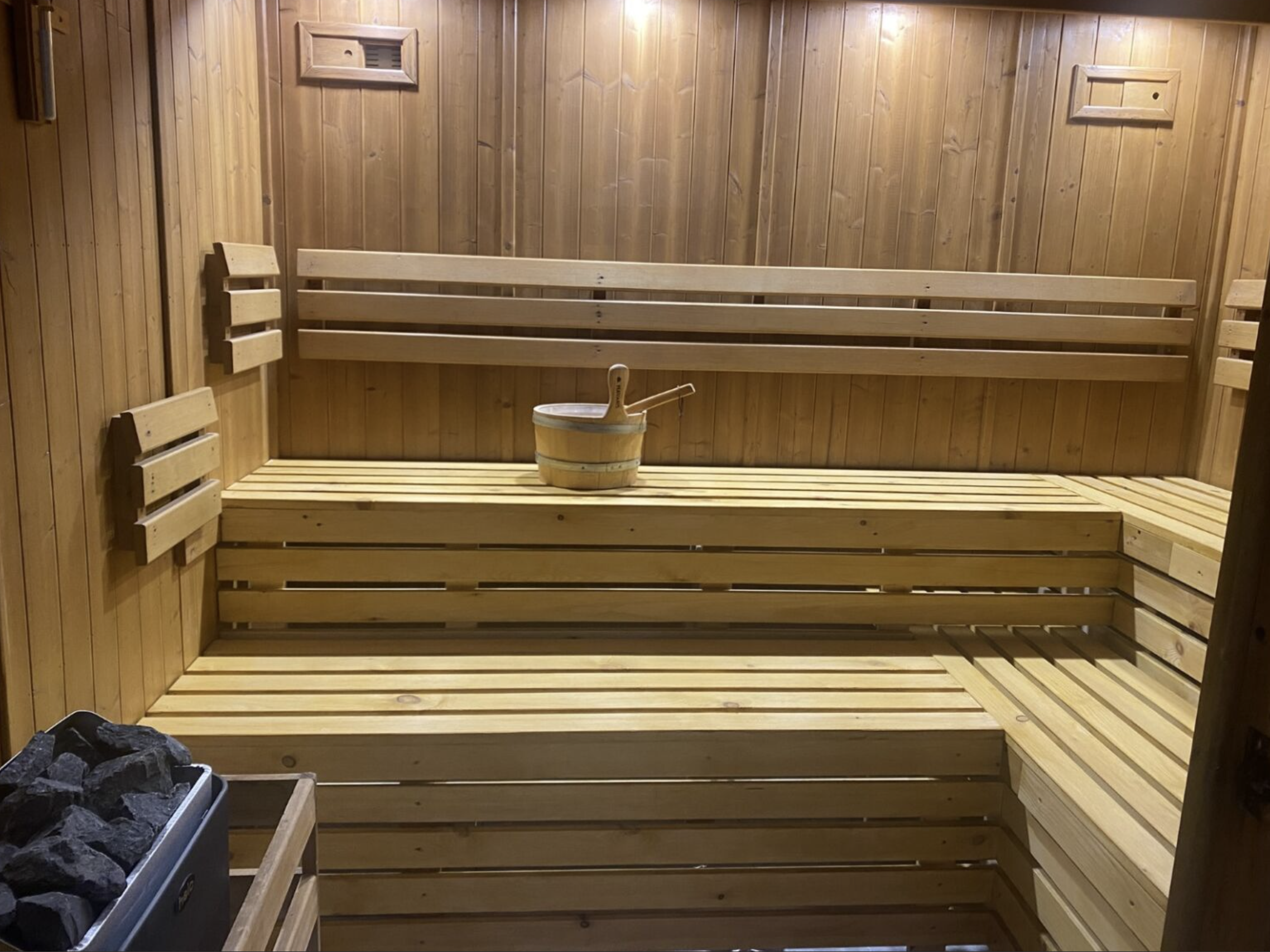 Wooden sauna interior with bench seating, a bucket with a ladle, and heated stones