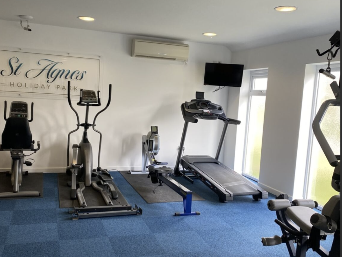 Small gym with cardio equipment including a treadmill, elliptical, rowing machine, and stationary bike at St Agnes Holiday Park.