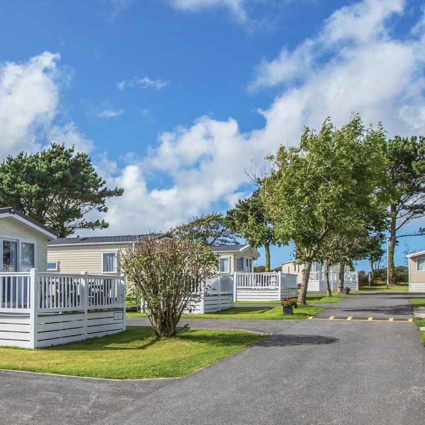 Several modern mobile homes with white decks and railings in a landscaped area with trees and a blue sky.
