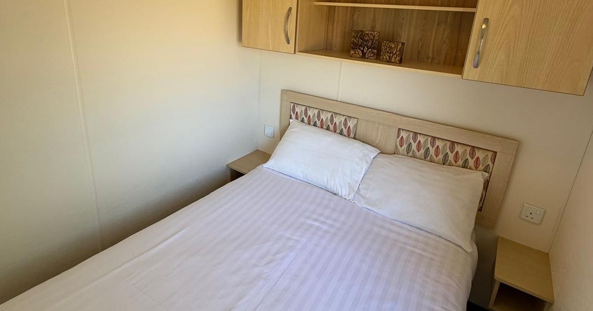 Small bedroom with a neatly made double bed, wooden shelves, and light-colored walls