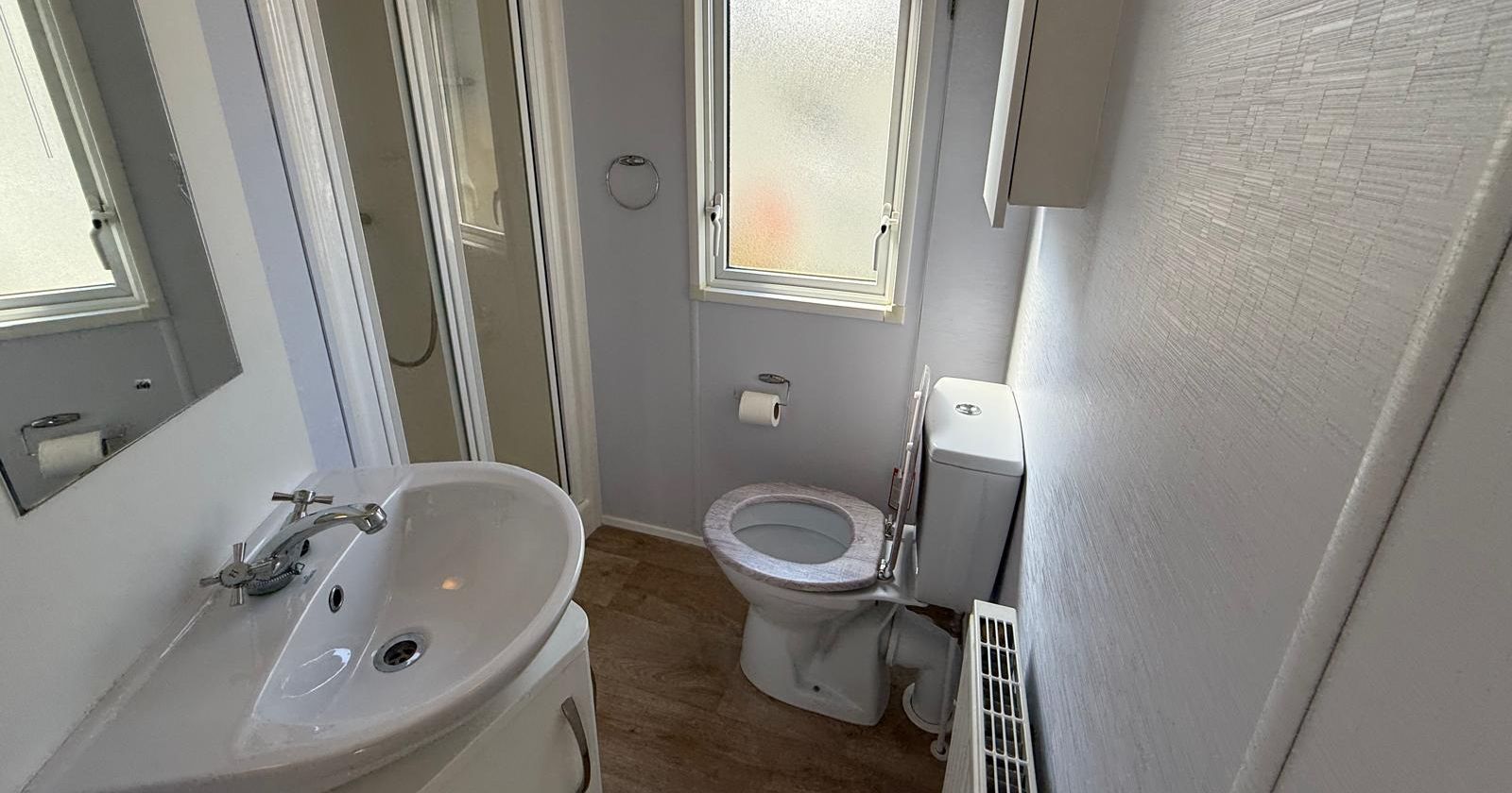 Small bathroom with a shower, sink, toilet, window, and radiator