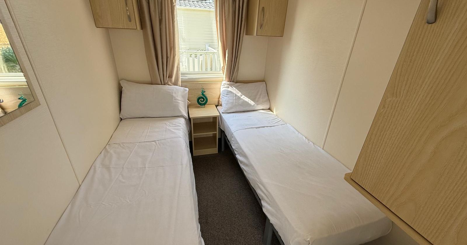 Small bedroom with two single beds, cream walls, and wood cabinets