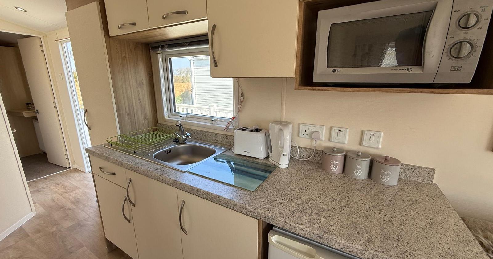 Compact modern kitchen with light-colored cabinets, a microwave, sink, mini fridge, and countertop appliances.