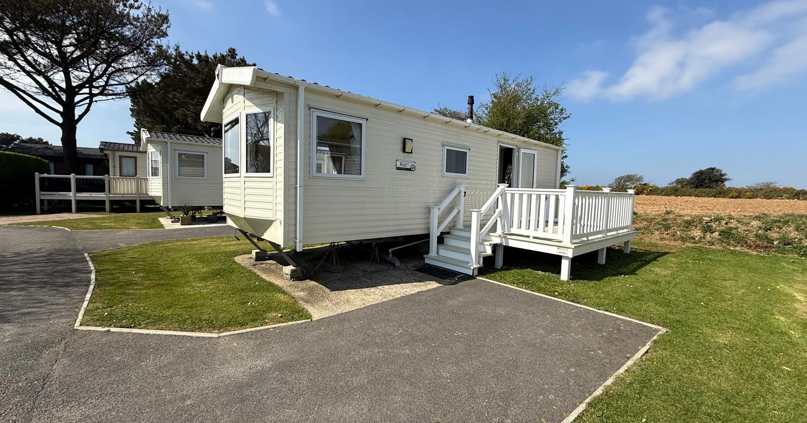 White static caravan with a small porch and steps, set in a holiday park with green grass and blue sky.