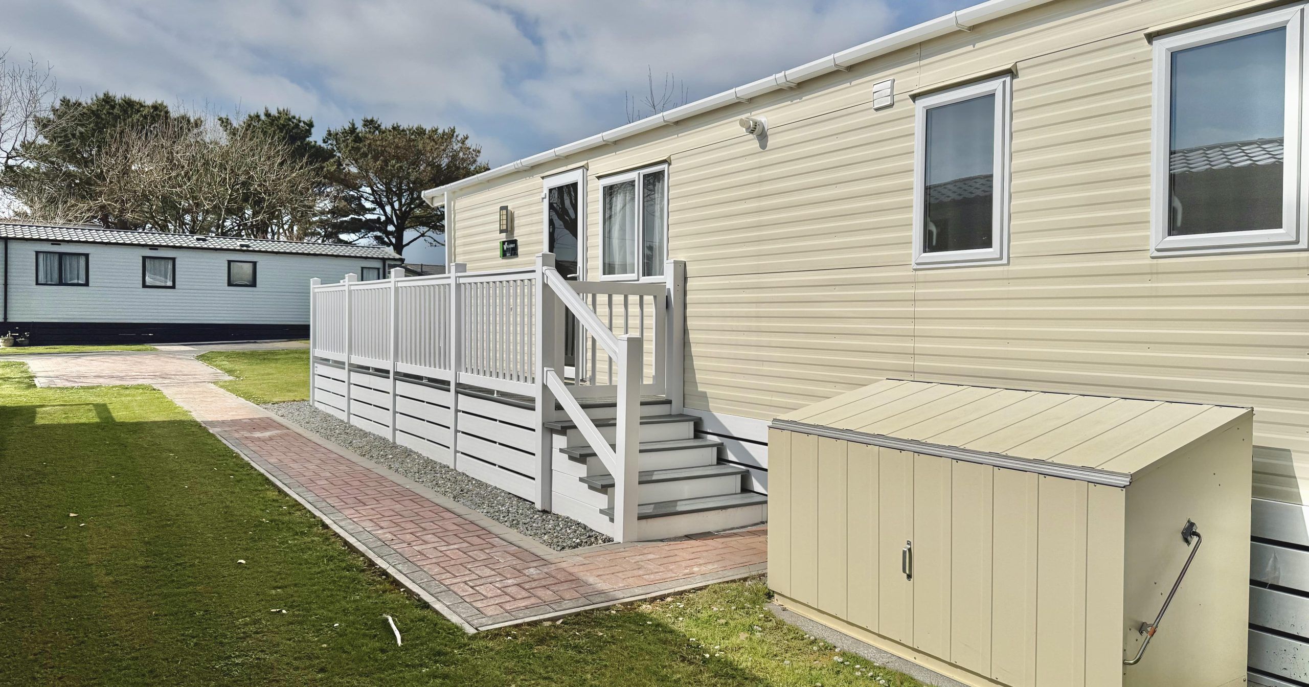 Modern mobile home with porch, side steps, and outdoor storage shed on a grassy lot