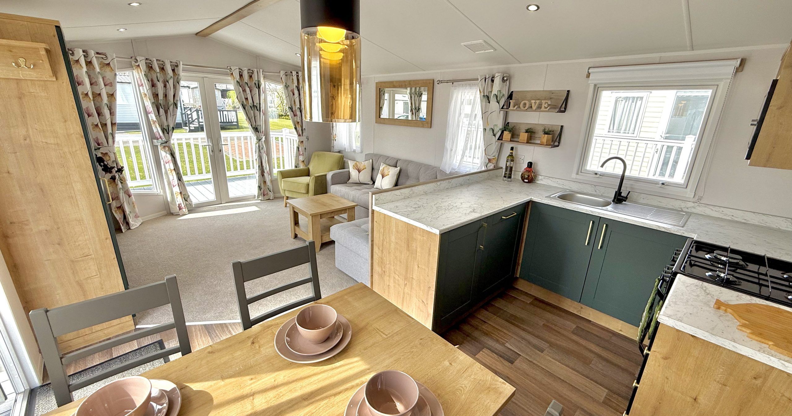 Modern open plan kitchen and living area in a mobile home with light wood furnishings and large windows.
