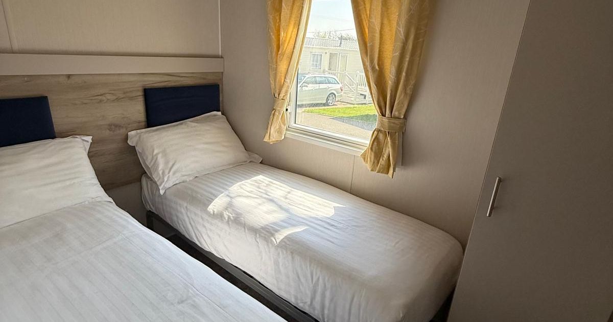 Small bedroom with two single beds and a window with yellow curtains