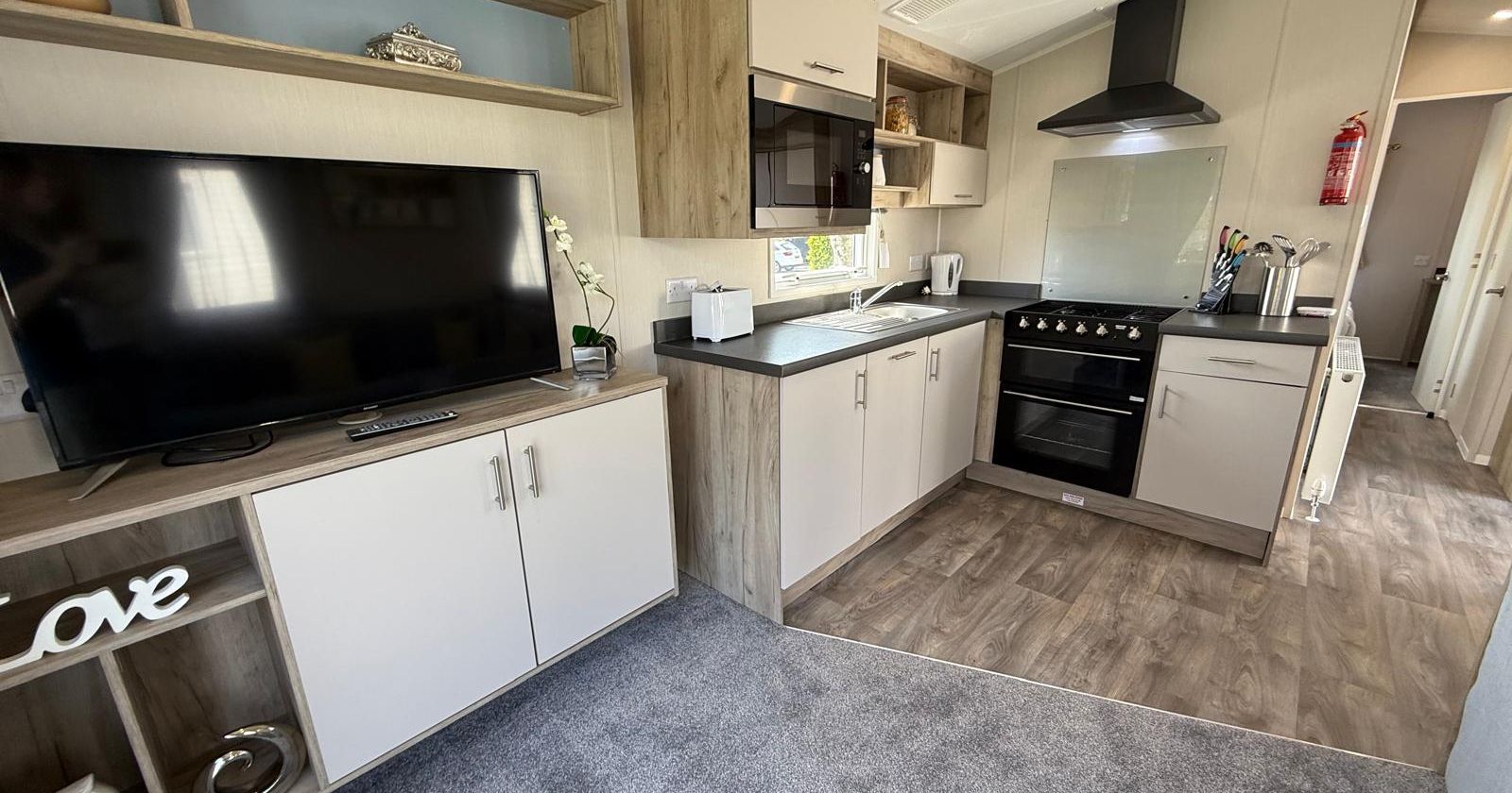 Modern kitchen and living area in a mobile home with a TV, oven, and cabinets.