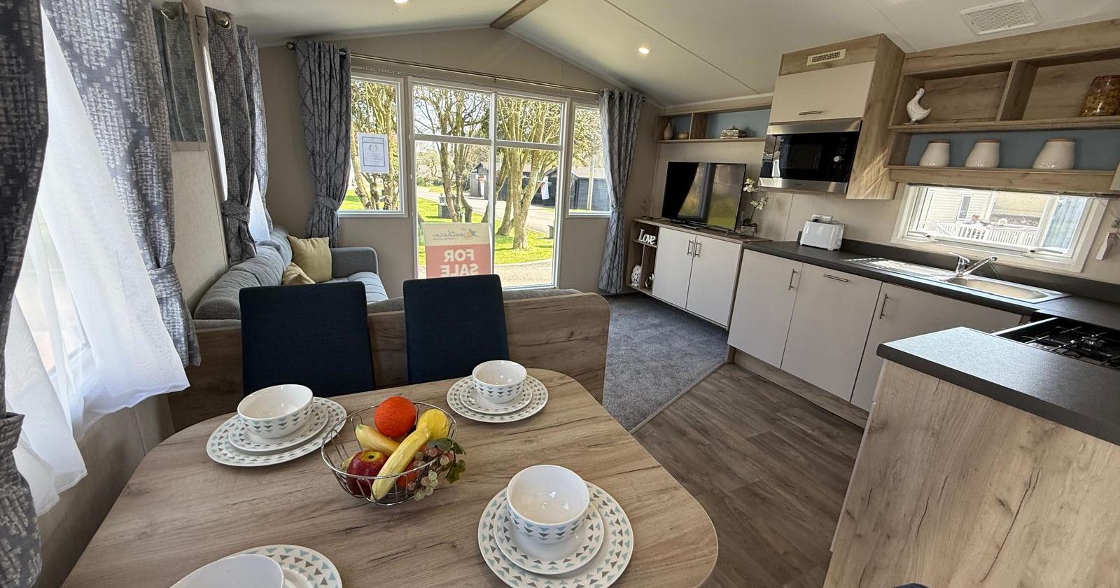 Modern mobile home interior with dining area, kitchen, living space, and large windows.