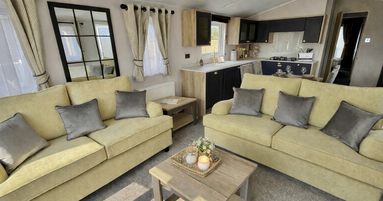 Modern living room and kitchen area with beige sofas, grey cushions, wooden table, and neutral decor