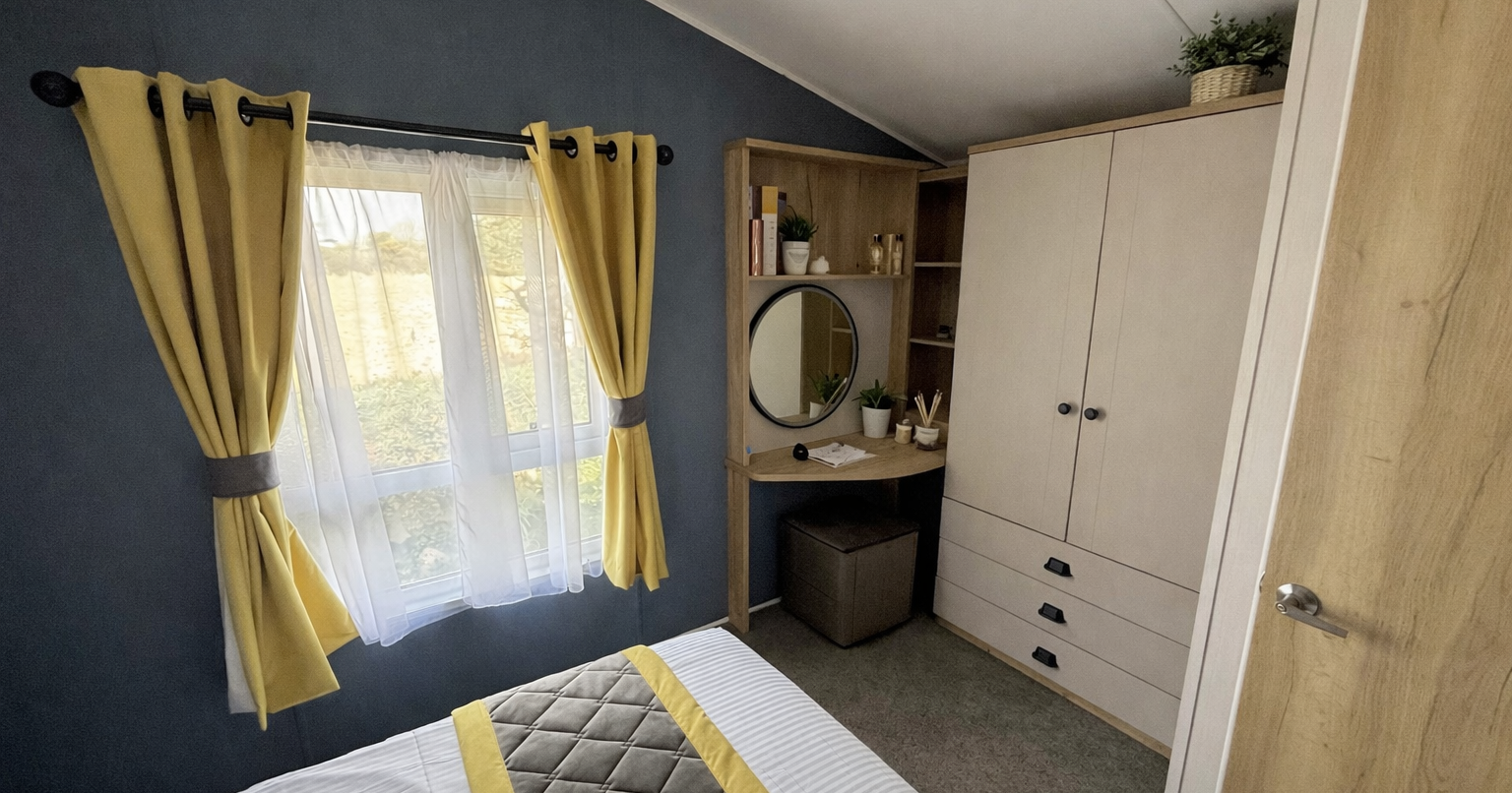 Cozy bedroom with yellow curtains, a bed, a wardrobe, and a wooden vanity with a round mirror.