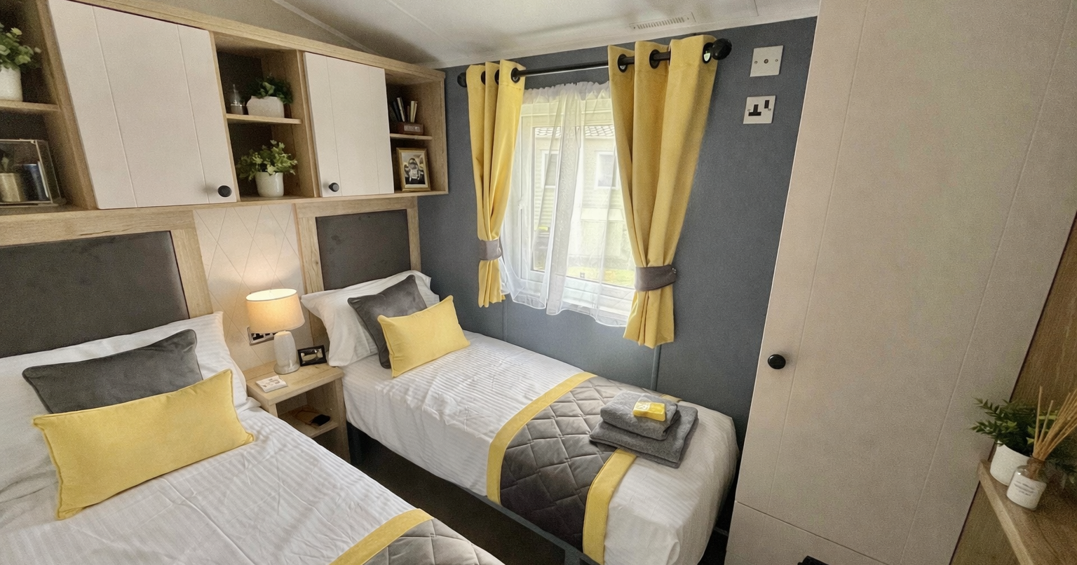 Modern twin bedroom with yellow and grey accents, two single beds, and a window with yellow curtains.