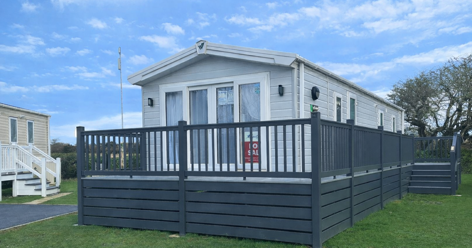 Modern mobile home for sale with a gray fence and decking