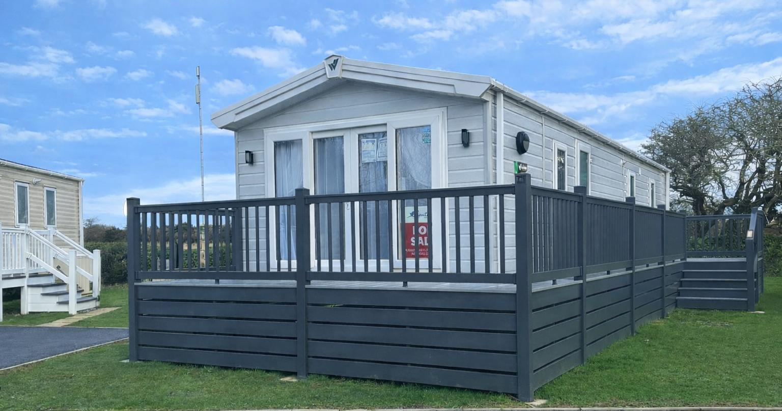 Modern mobile home for sale with a gray fence and decking