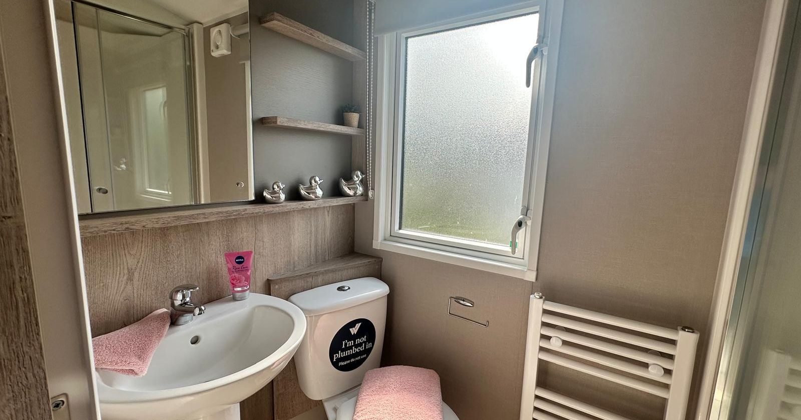 Compact bathroom with pedestal sink, toilet, frosted window and heated towel rail