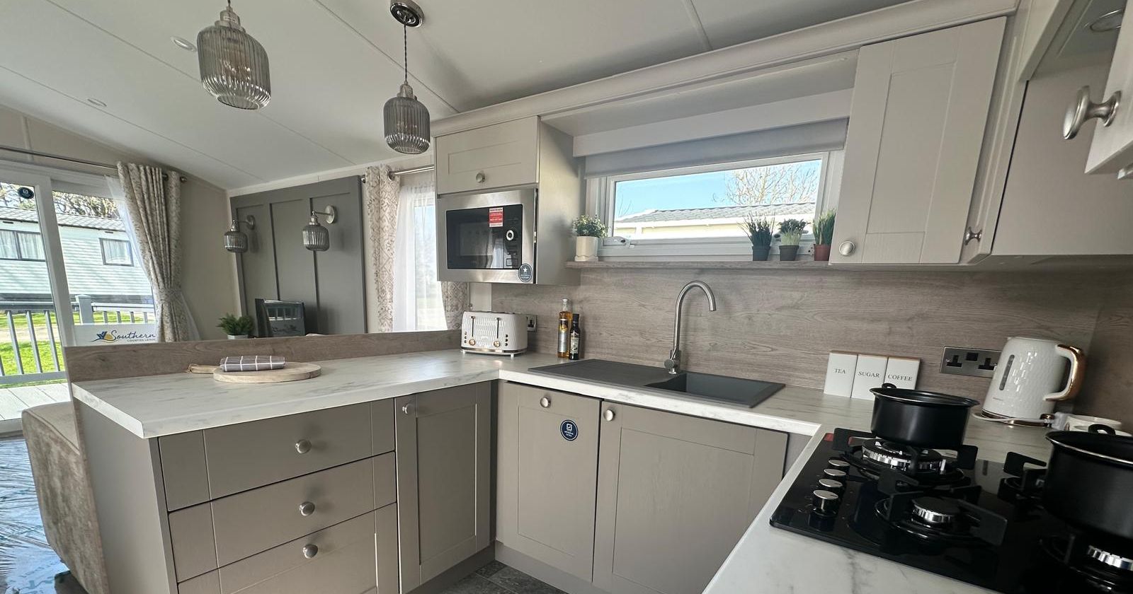 Modern caravan kitchen with grey cabinets, marble-effect worktops, black sink and four-burner gas hob, with microwave and pendant lights