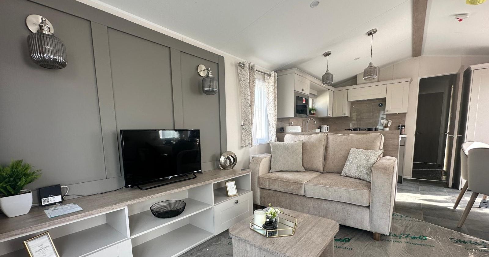 Modern open-plan living room with grey feature wall, TV unit, beige sofa and compact kitchen in the background