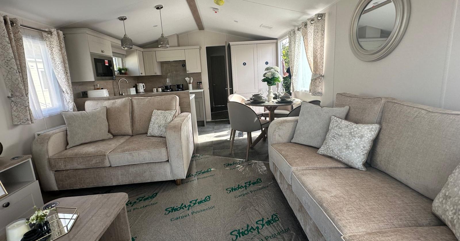 Bright open-plan living room with beige sofas, dining table and modern kitchen in a static caravan