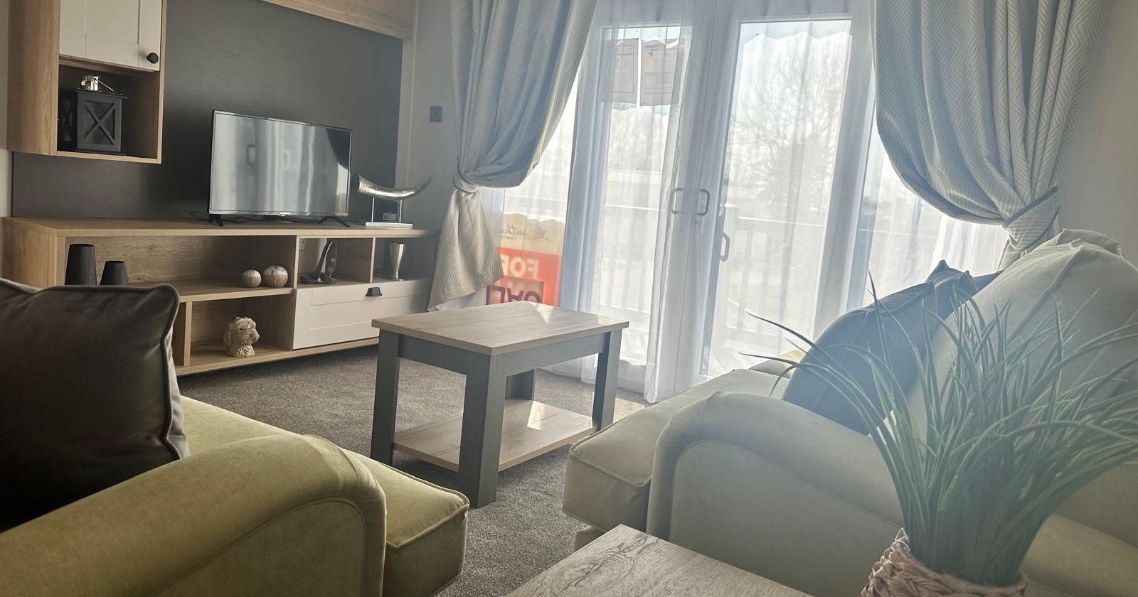 Cosy living room with sofas, coffee table, TV unit and large patio doors with curtains