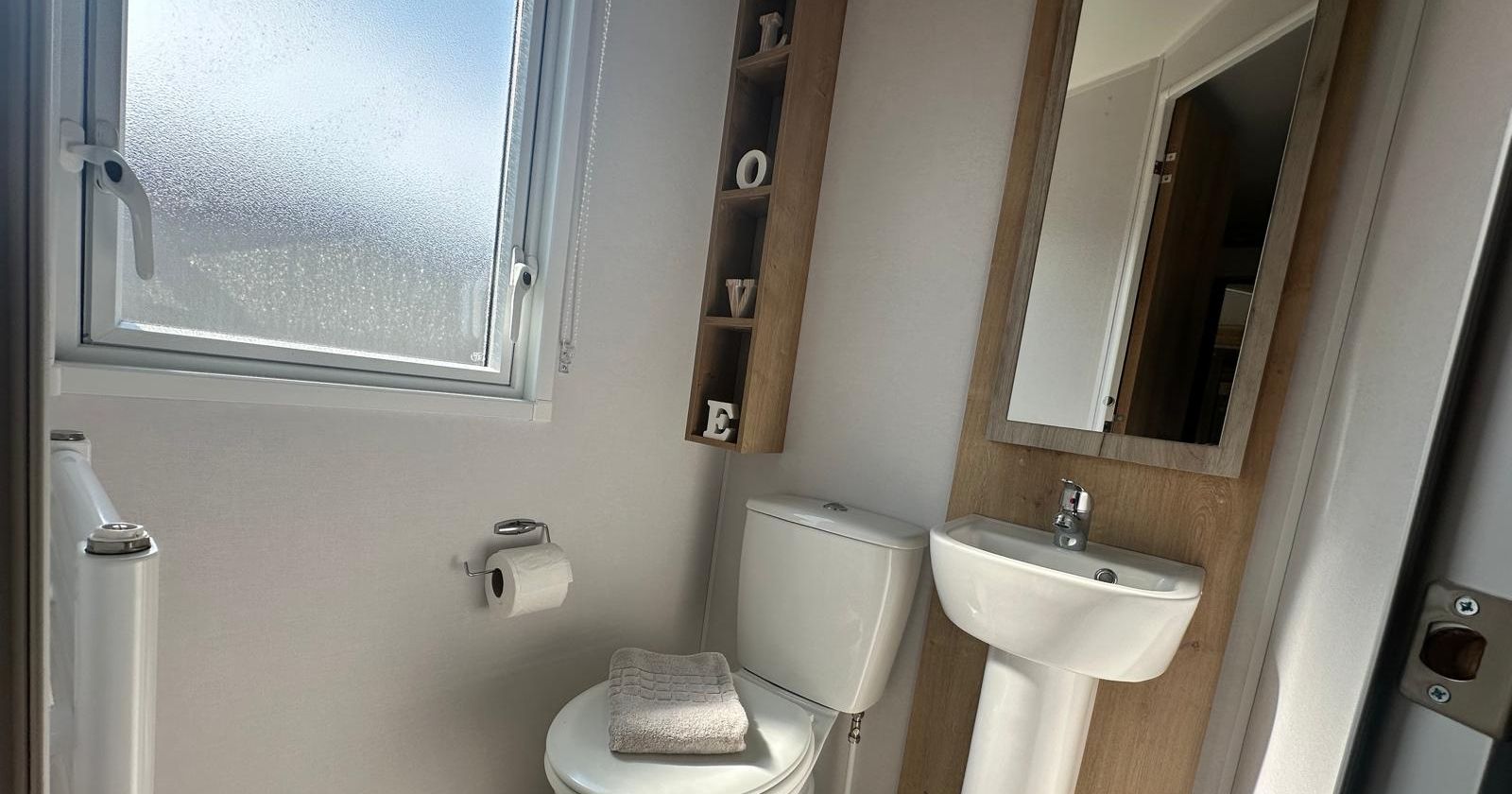 Compact bathroom with toilet, pedestal sink, wall mirror, frosted window and geometric patterned floor tiles