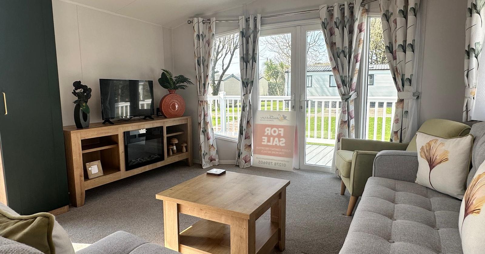 Bright, modern living room with grey sofa, wooden coffee table, TV unit and patio doors with floral curtains