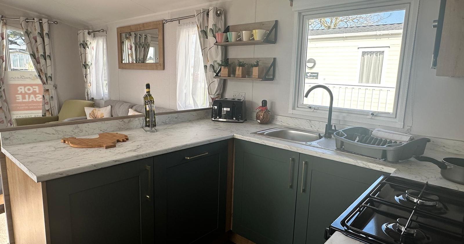 Modern caravan kitchen with dark green cabinets, marble-effect worktop, sink and gas hob by a window
