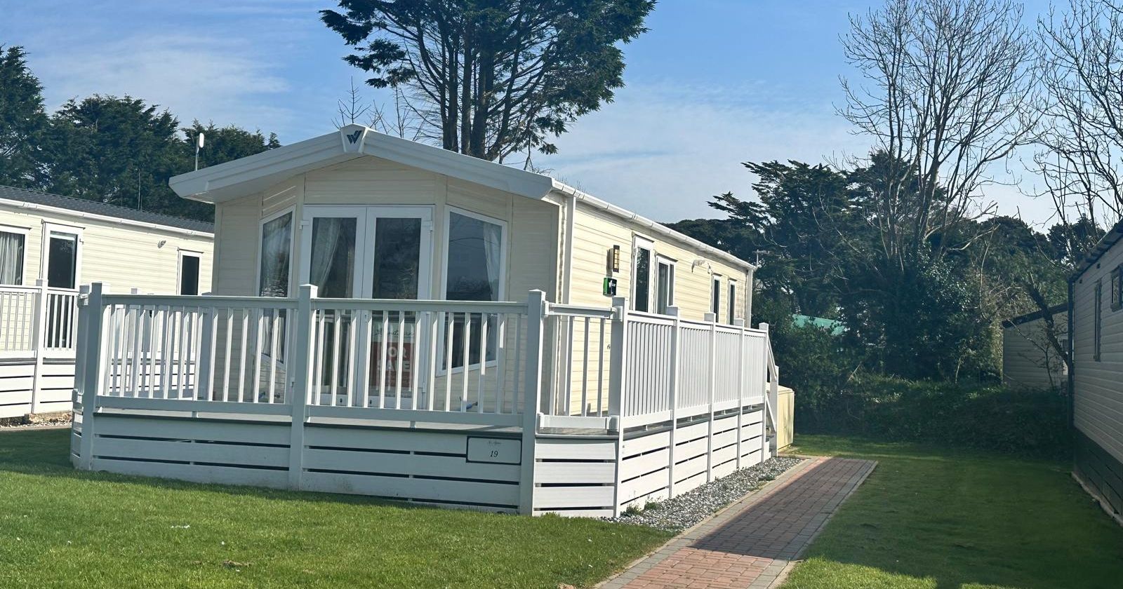 Cream static caravan with white decking and railings on a grassy holiday park under a blue sky