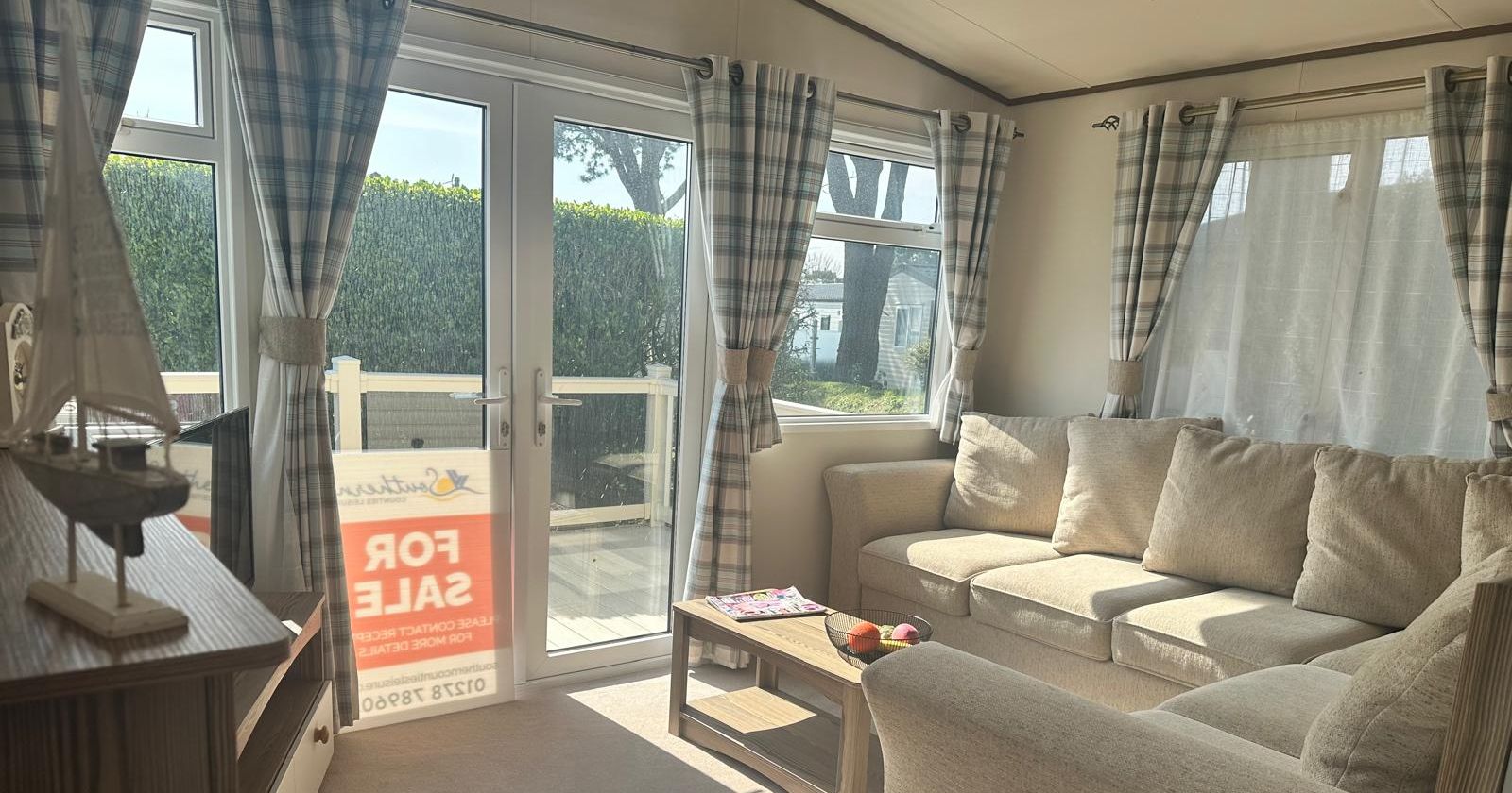 Sunlit living room with beige sofa, wooden coffee table and French doors with blue plaid curtains