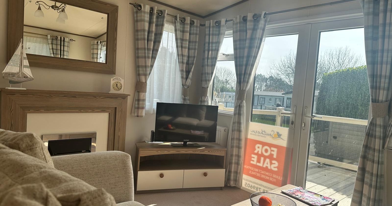 Bright caravan living room with plaid curtains, TV, coffee table and French doors leading to a deck