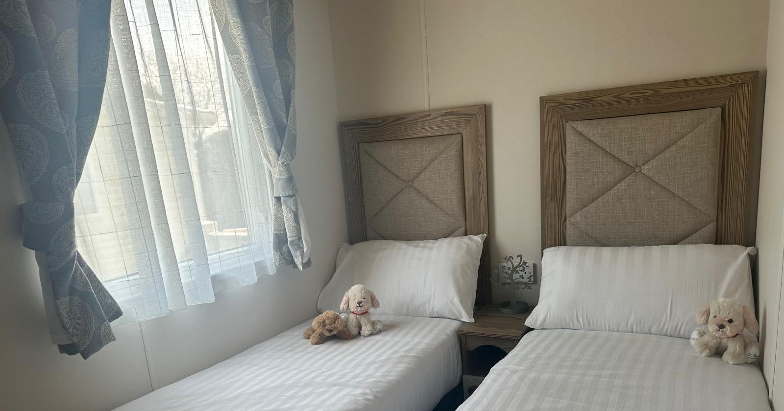 Twin bedroom with two single beds, white striped bedding, blue curtains and soft toy dogs on the pillows
