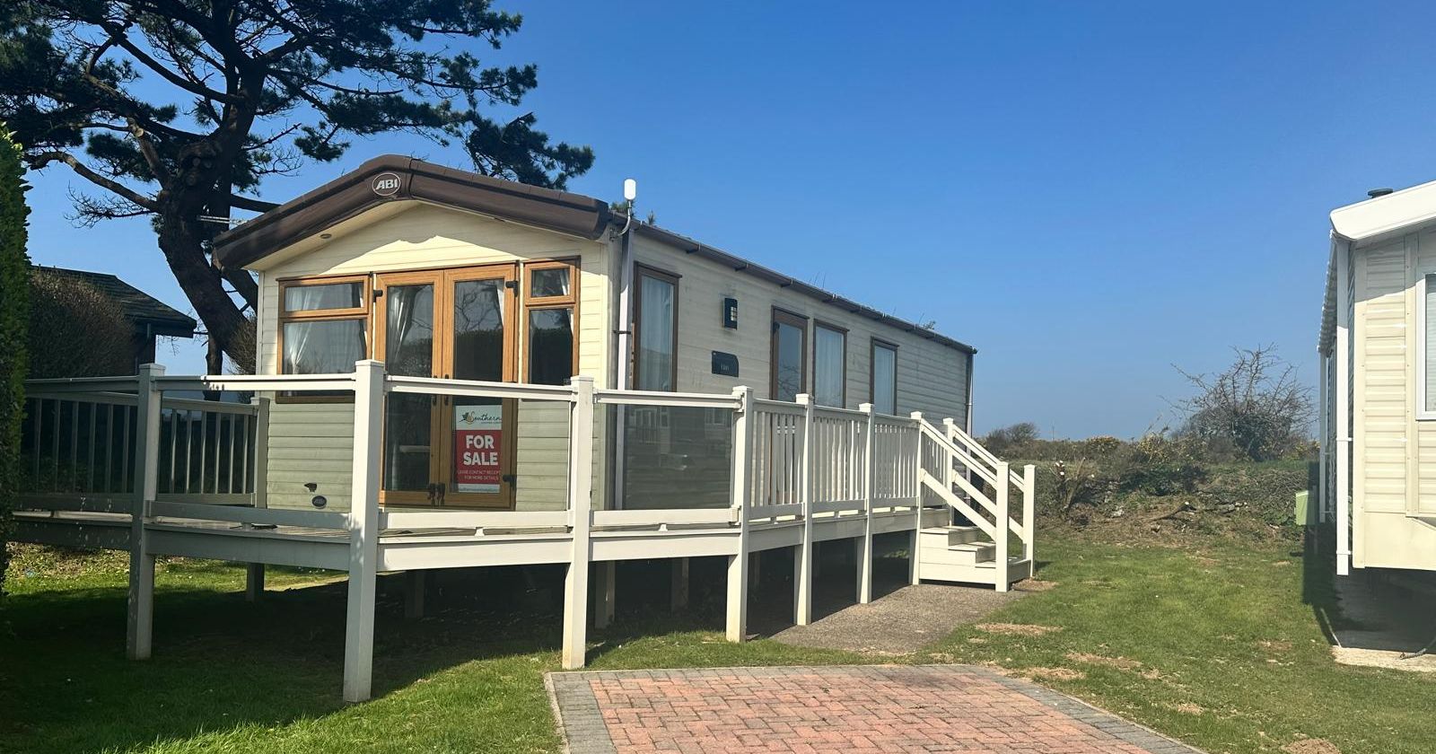 Static caravan with raised deck and steps beside a brick-paved driveway on a sunny day