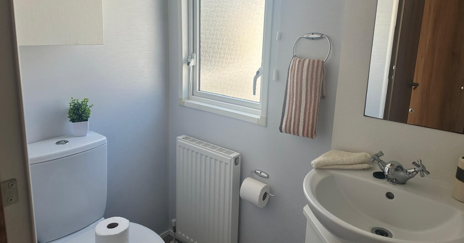 Small bathroom with white toilet, pedestal sink, mirror and frosted window