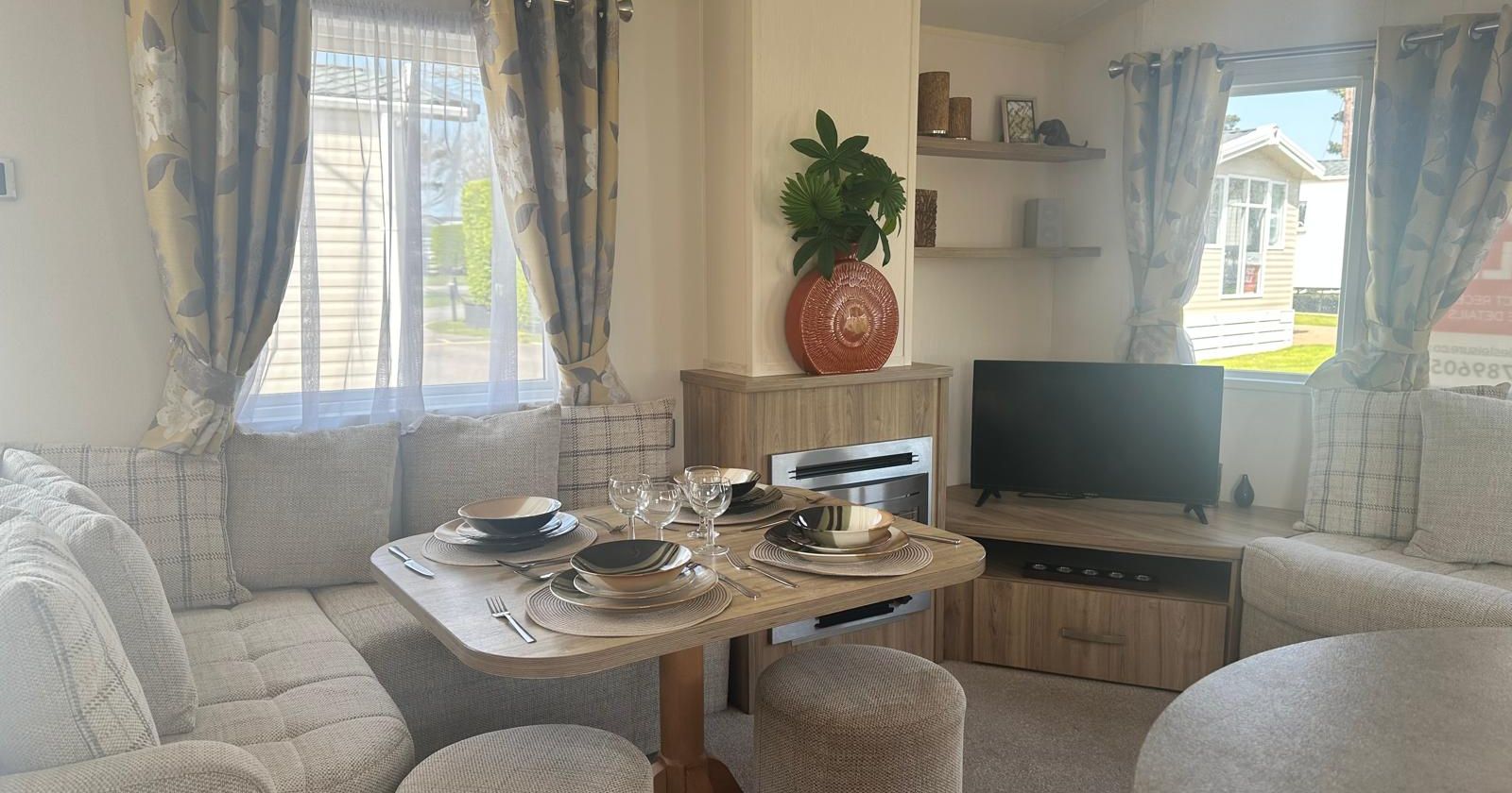 Cosy caravan living area with corner sofa, dining table set for four, and TV by the window