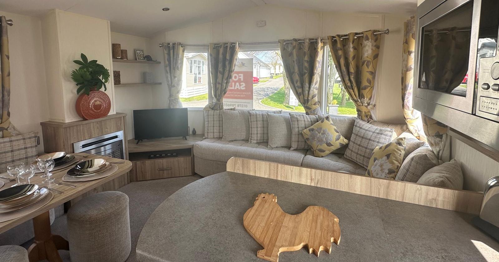 Cosy static caravan lounge and dining area with corner sofa, TV, and patterned curtains