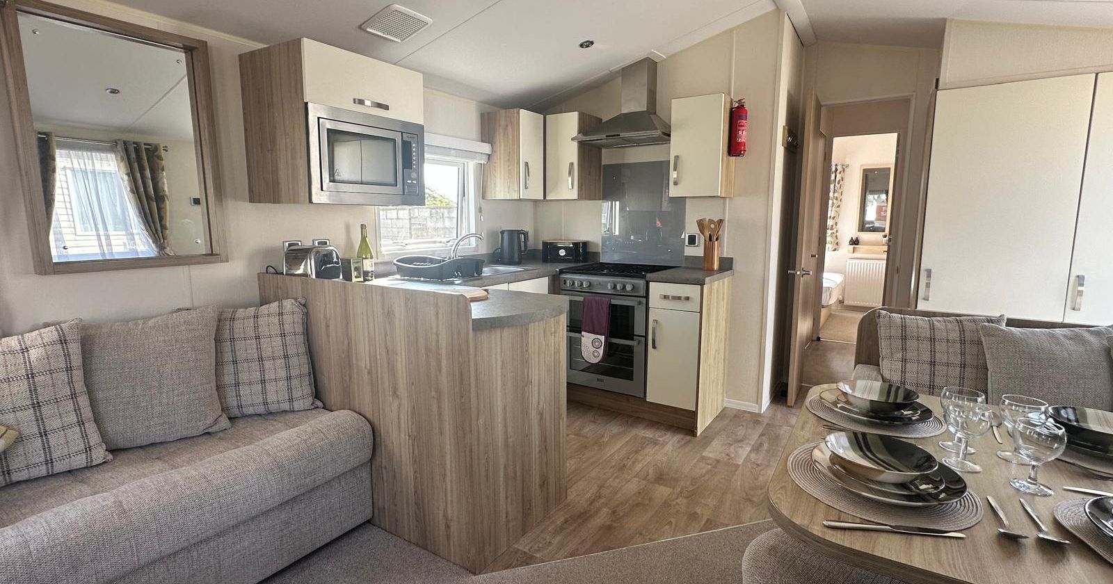 Modern open-plan caravan living area with fitted kitchen, grey sofa and dining table set for four